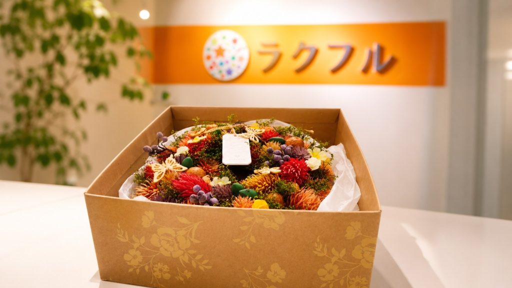 受付に飾られた彩り豊かなプリザーブドフラワーのギフトとラクフルのロゴ